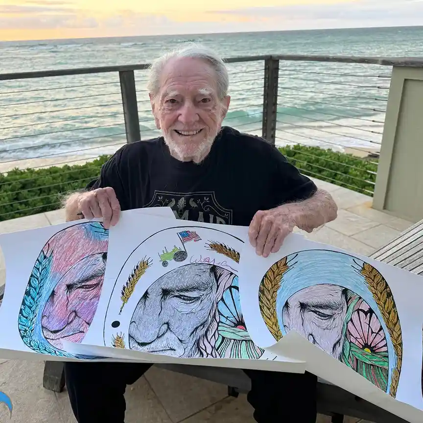 An elderly man with white hair and a beard smiles while holding up three colorful, detailed drawings of his own face, each…