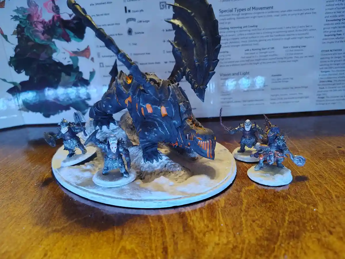 A large, dark blue dragon miniature with glowing orange accents is posed on a circular base with snow-like texture…