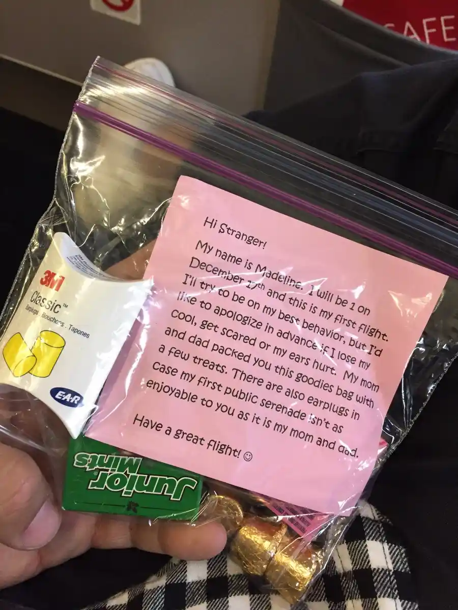A hand holds a clear plastic zip-top bag containing a pink handwritten note, a package of 3M Classic earplugs, and Junior…