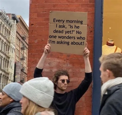 A man with curly hair and sunglasses holds up a cardboard sign with black text that reads: 'Every morning I ask, "Is he dead…