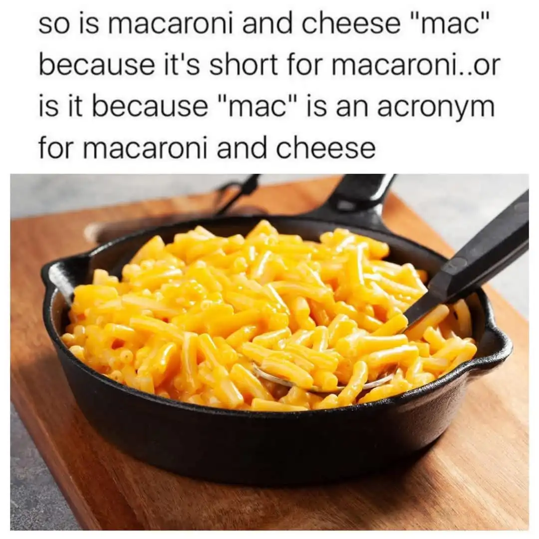 A black cast-iron skillet filled with creamy yellow macaroni and cheese sits on a wooden cutting board, with a black-handled…