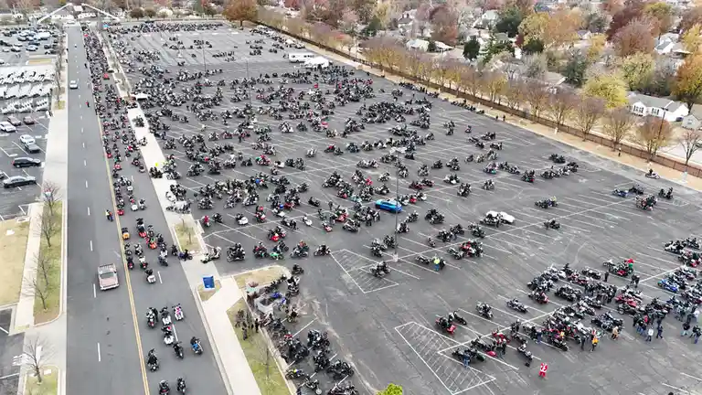 An aerial view shows a massive parking lot filled with hundreds of motorcycles and riders, with a single person dressed as…