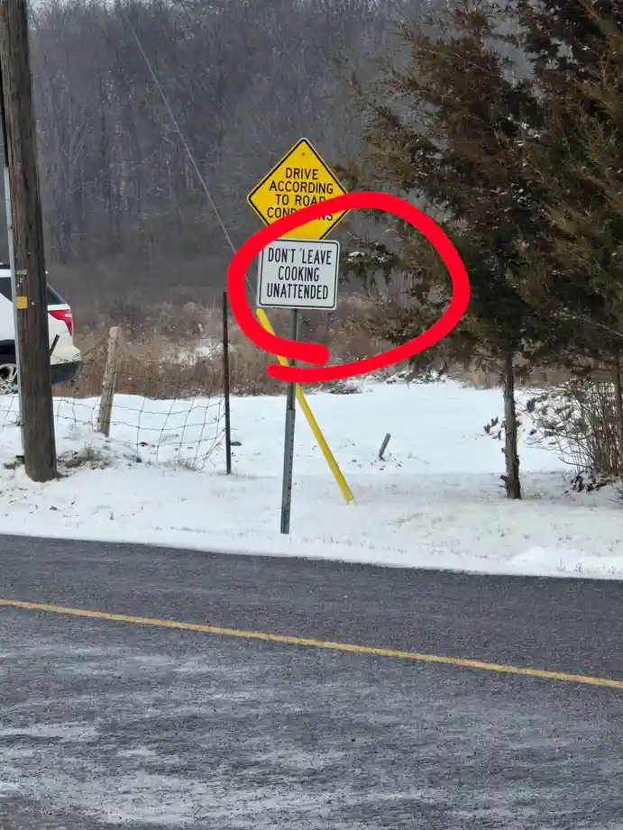 A snowy roadside scene shows two signs: a yellow diamond-shaped warning sign reading 'DRIVE ACCORDING TO ROAD CONDITIONS'…