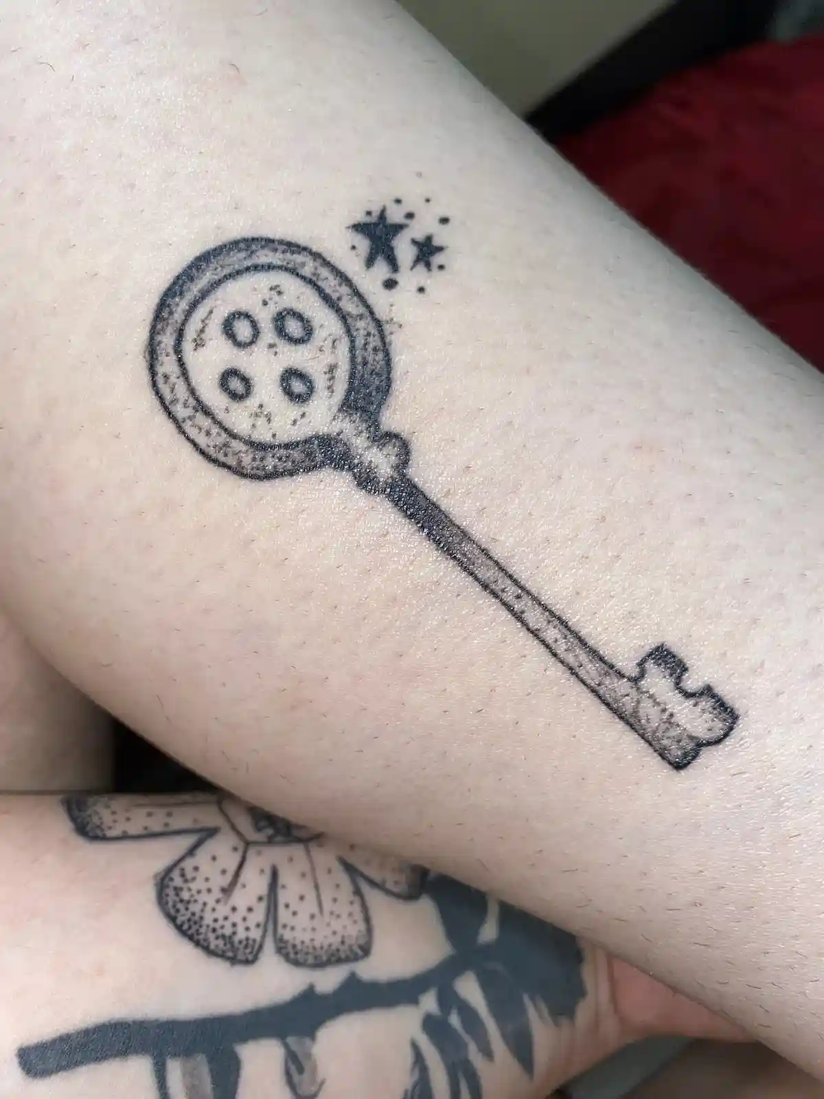 A close-up photo shows a black ink tattoo on a person's inner forearm, depicting a stylized key with a circular head shaped…