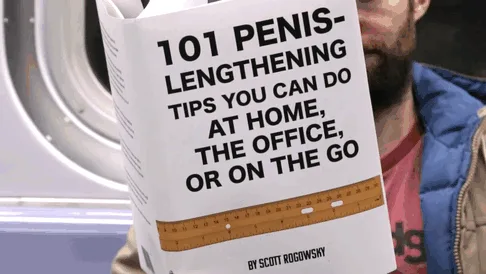 A man on a subway holds up a book titled '101 Penis-Lengthening Tips You Can Do At Home, The Office, Or On The Go' by Scott…