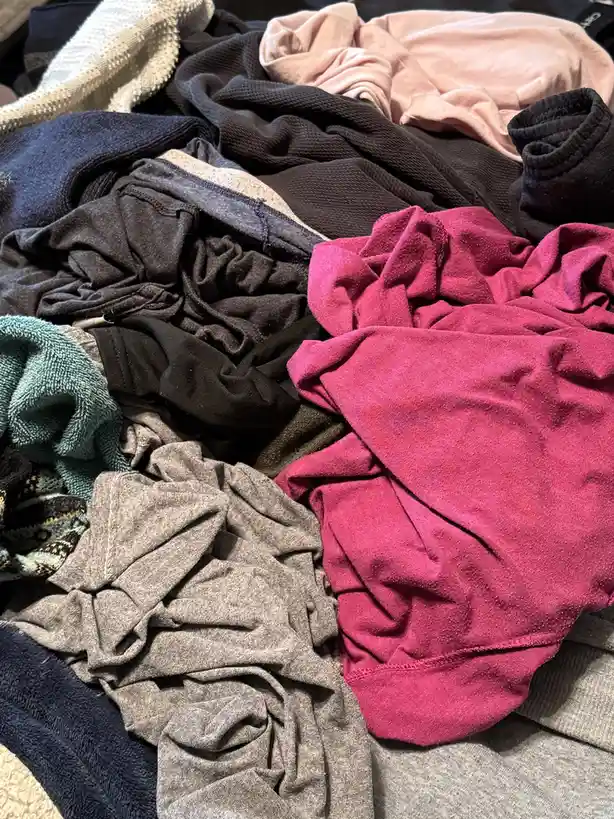 A close-up photo shows a large, messy pile of freshly washed, crumpled clothes in various colors including pink, gray…
