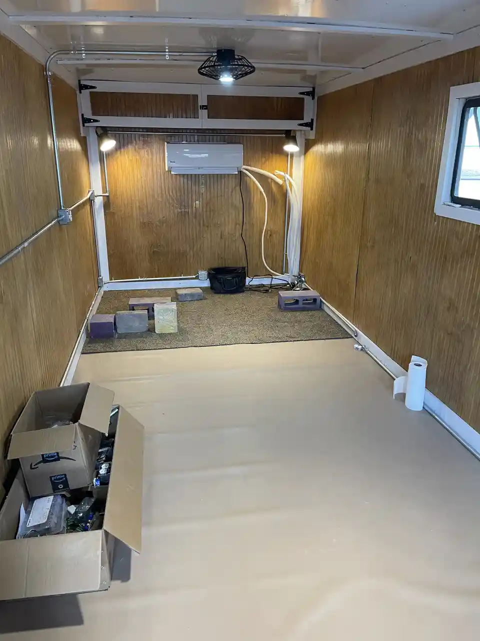 An interior view of an rv or trailer under renovation, showing wood-paneled walls, a partially installed air conditioner…