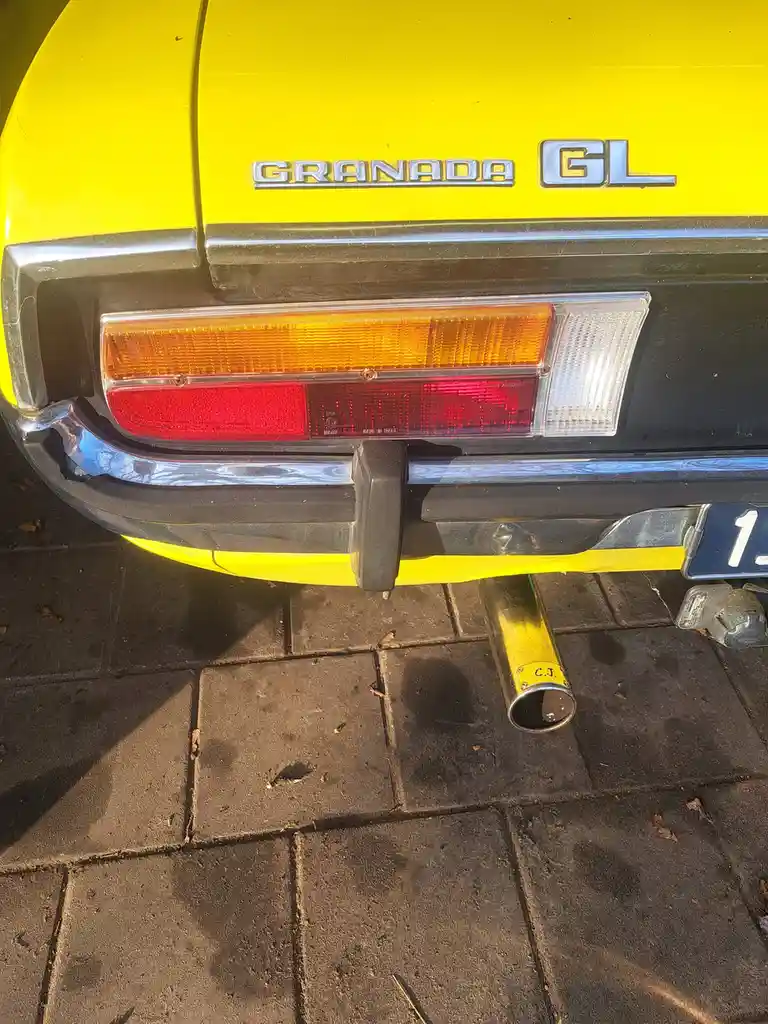 A close-up of the rear of a bright yellow vintage Ford Granada GL, showing its taillights, bumper, and a custom-painted…