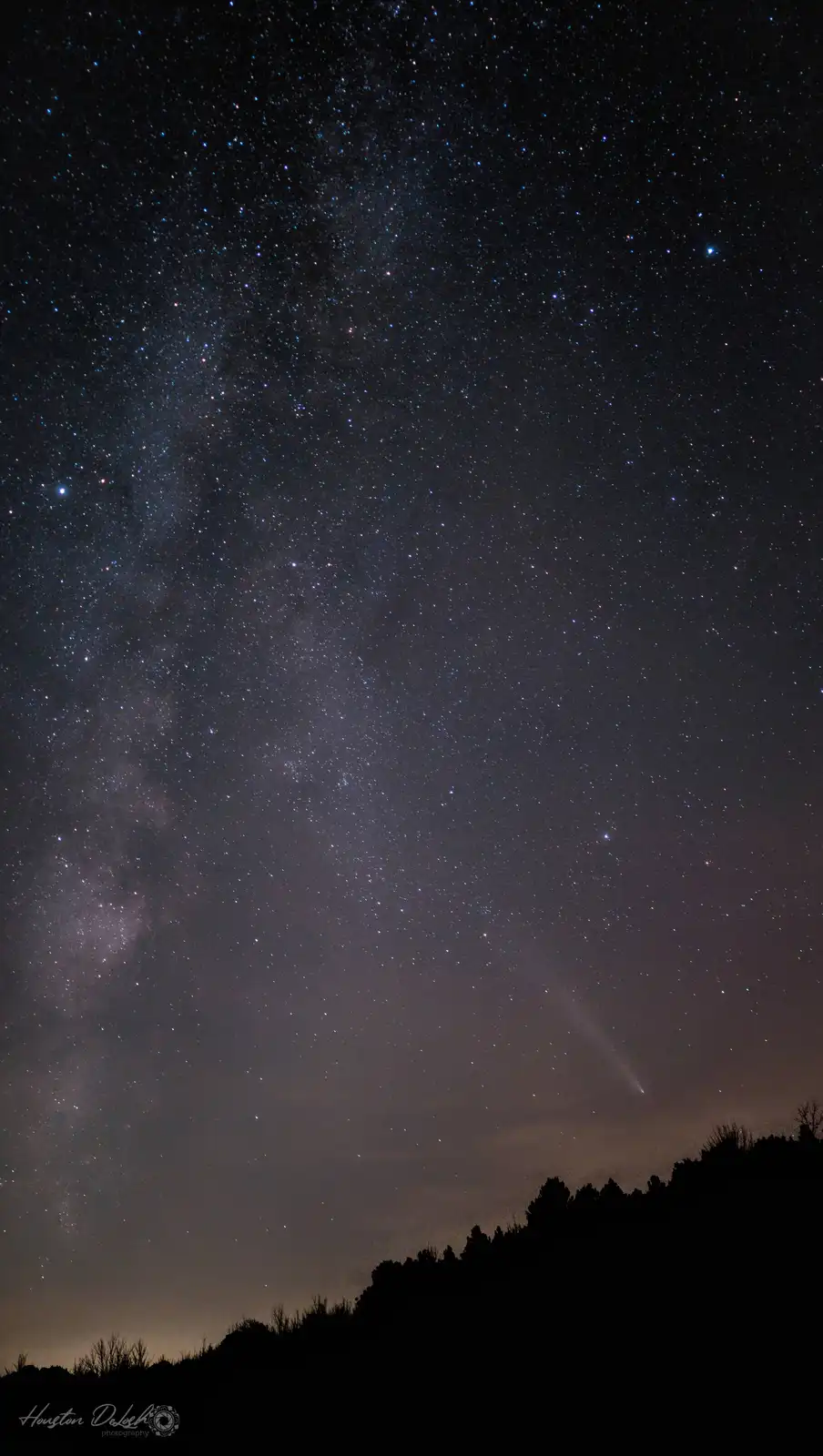 A stunning night sky photograph shows the Milky Way galaxy stretching diagonally across a dark sky filled with countless…