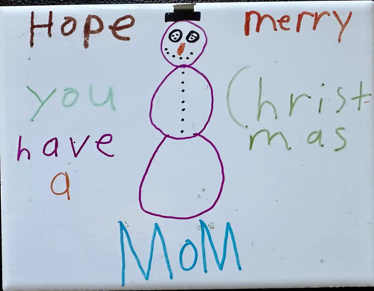 A child's hand-drawn snowman with a top hat and carrot nose is centered on a white surface, surrounded by colorful…