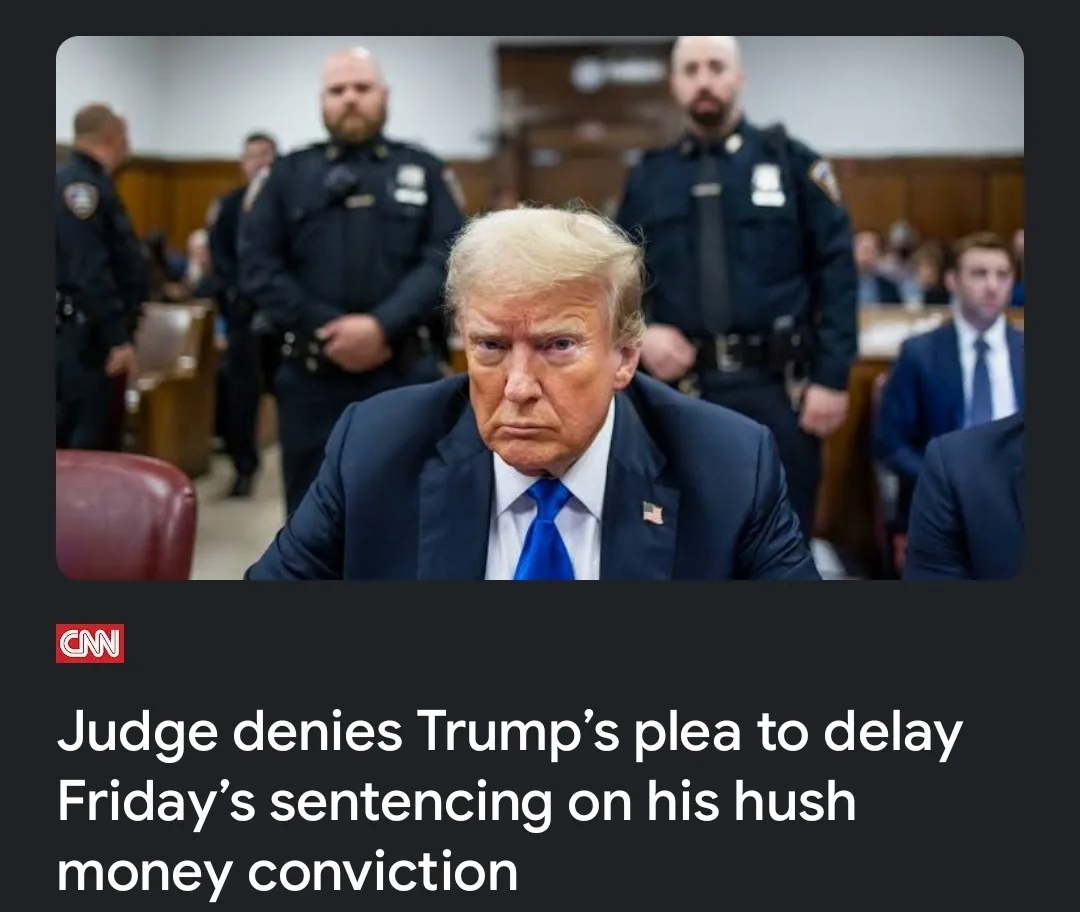 A photo of Donald Trump sitting in a courtroom with a stern expression, flanked by two uniformed police officers standing…