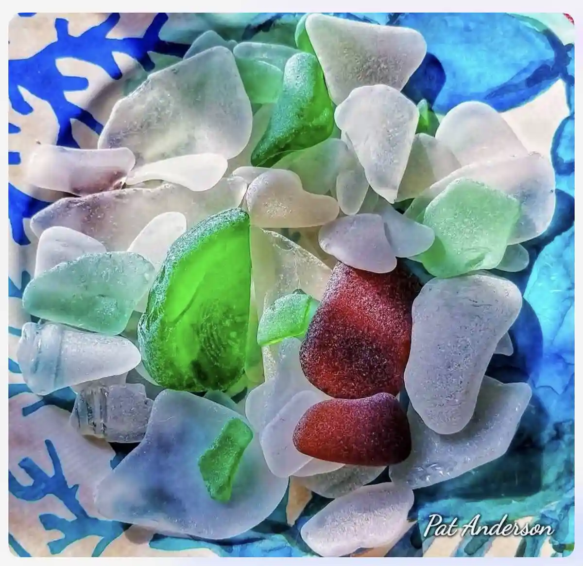 A close-up photo of assorted sea glass pieces in shades of green, white, and red, arranged on a blue and white patterned…