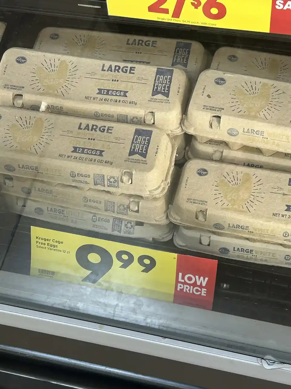 A close-up of Kroger brand egg cartons in a refrigerated grocery store aisle, labeled 'CAGE FREE' and 'LARGE WHITE EGGS'. A…