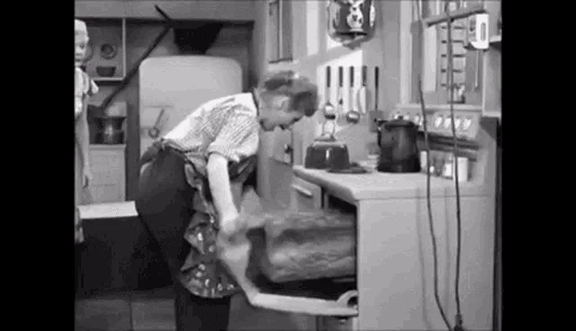 A black-and-white sequence from an old TV show shows a woman struggling to move a large log across a kitchen counter, while…