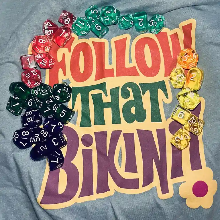 A gray t-shirt with a large, colorful graphic that reads 'FOLLOW THAT BIKINI!' in red, green, and purple stylized letters…