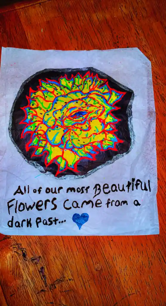 A child's hand-drawn artwork on white paper shows a vibrant, psychedelic-style flower with yellow, green, and red colors…
