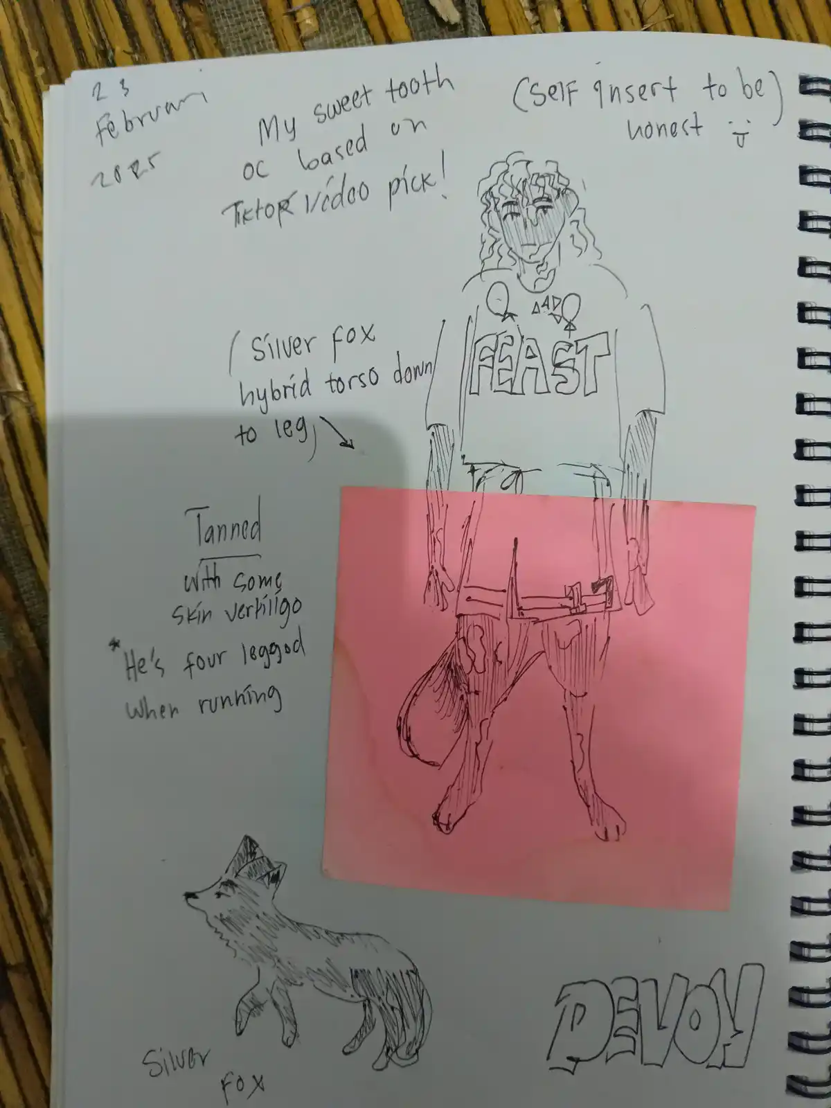 A hand-drawn sketch in a spiral notebook shows a humanoid figure with fox-like features, wearing a shirt that says 'FEAST'…
