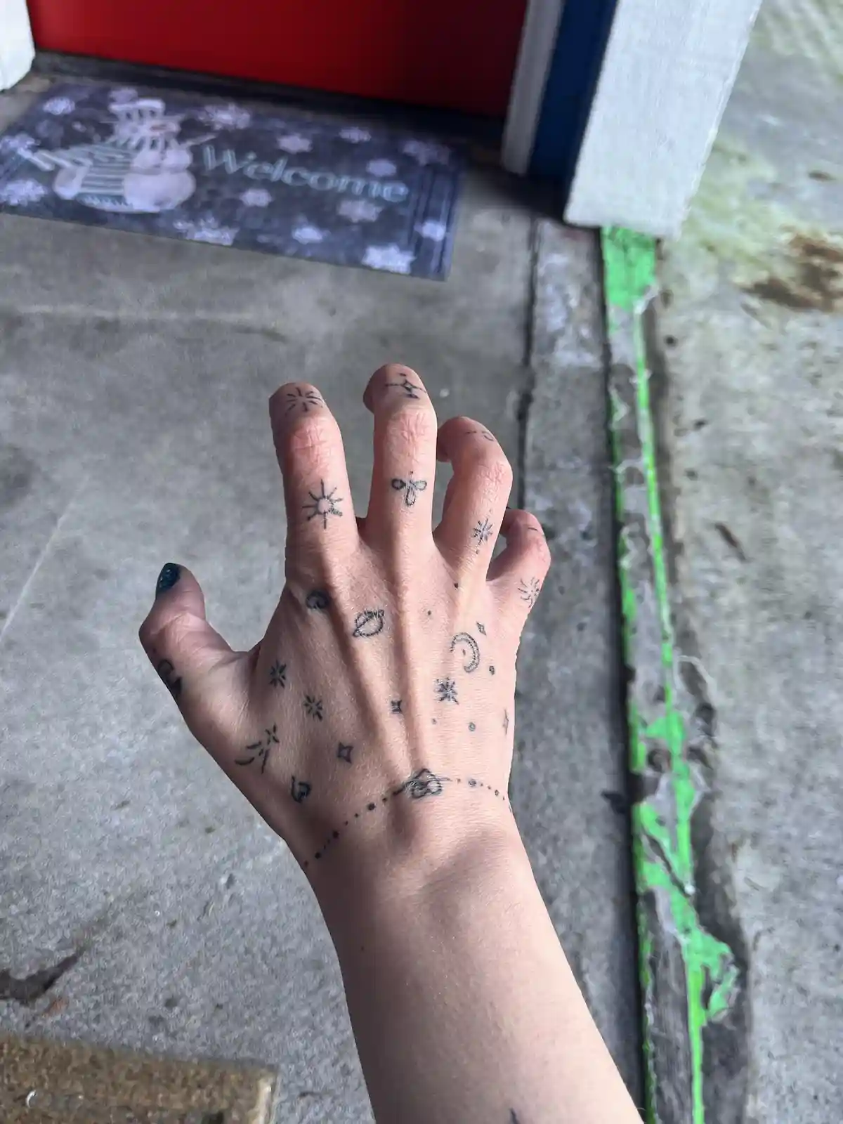 A close-up photo shows a person's hand with small, black ink tattoos of celestial bodies like the sun, moon, planets, and…