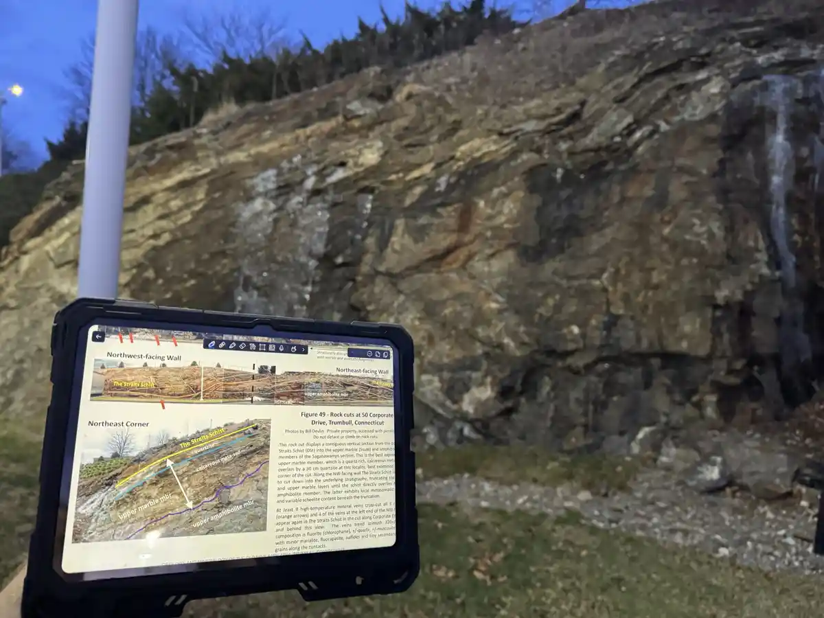 A person holds a tablet displaying a detailed geological diagram labeled 'Figure 49 - Rock cuts at 50 Corporate Drive…