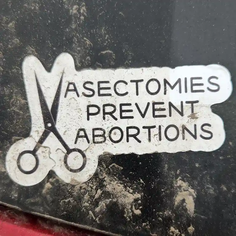 A weathered white sticker on a dirty black surface features a black silhouette of scissors and the text 'ASECTOMIES PREVENT…