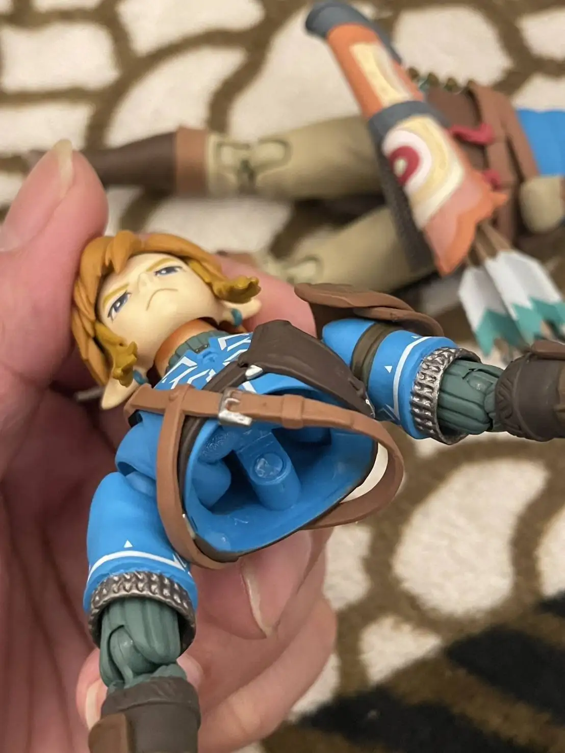 A close-up photo shows a person's hand holding a Link action figure from The Legend of Zelda: Breath of the Wild. The figure…