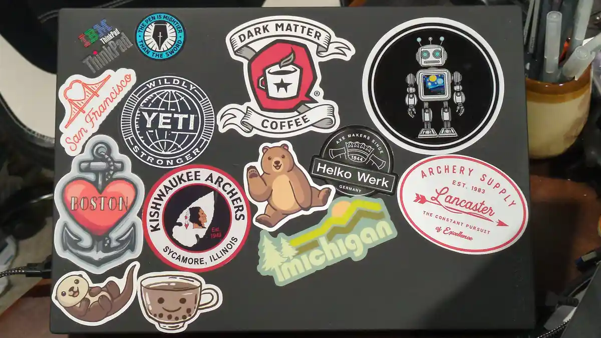 A black laptop lid is covered in numerous colorful stickers, including 'San Francisco', 'Boston', 'Yeti', 'Dark Matter…