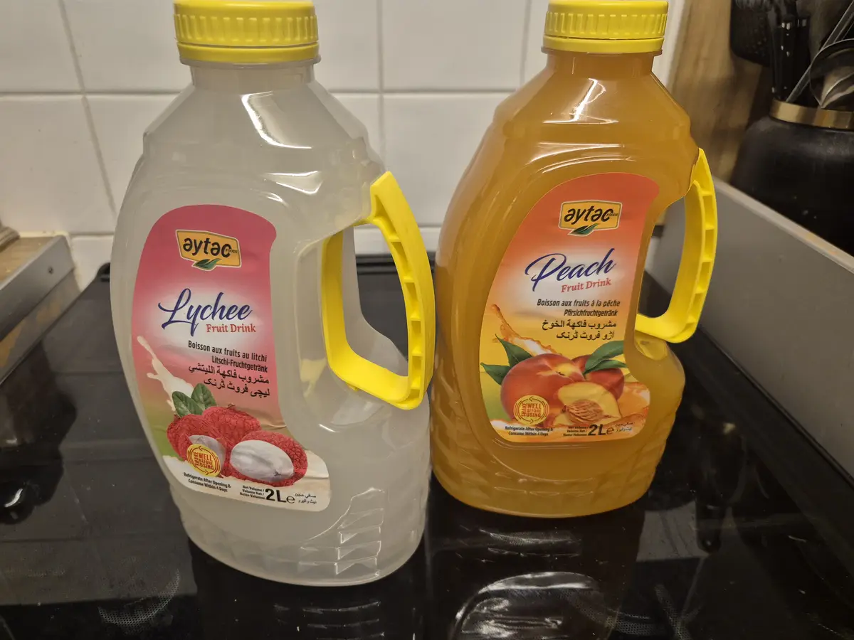 Two large 2-liter plastic bottles of Aytac brand fruit drink sit side-by-side on a black stovetop. The bottle on the left is…