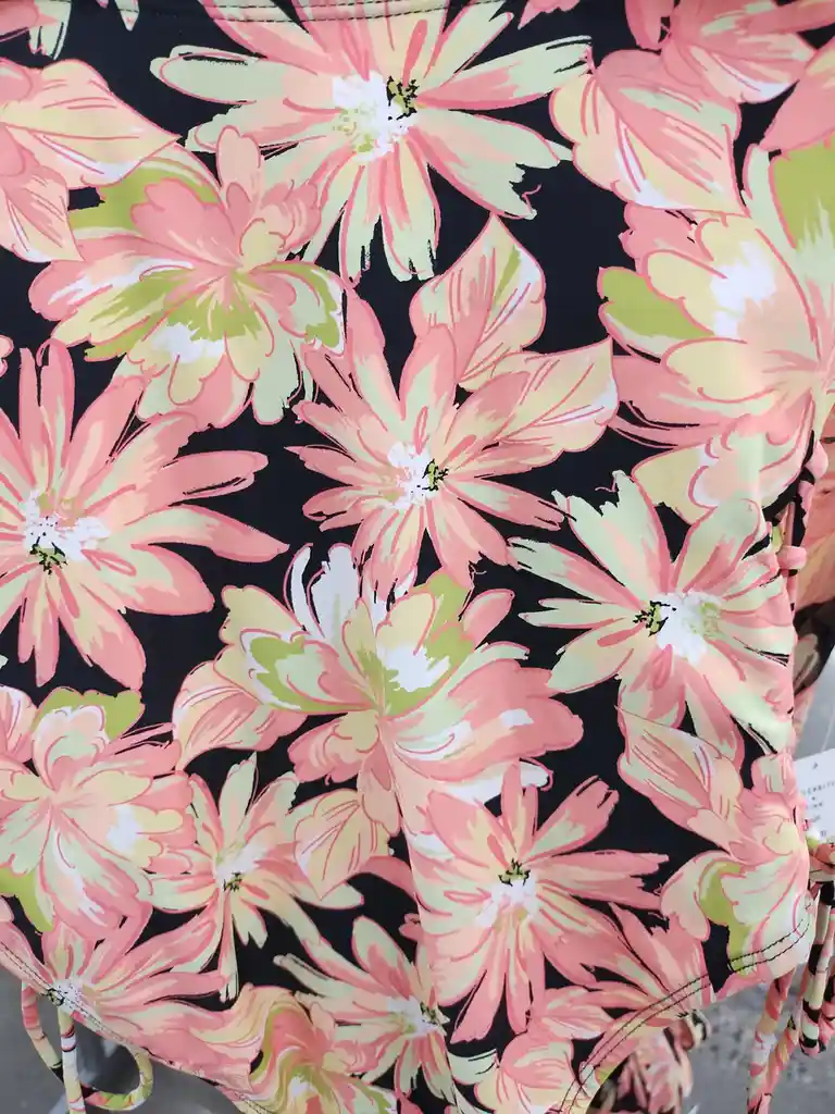 A close-up of a black fabric with a bold, repeating floral pattern featuring large pink, yellow, and green flowers. The…