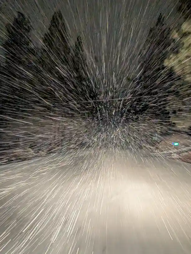 A long-exposure photograph captures streaks of falling snow radiating outward from a central point, creating a tunnel-like…