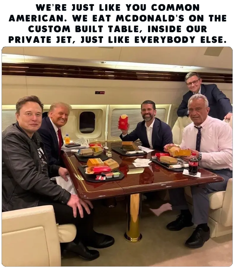 Five men are seated around a large, custom-built wooden table inside a private jet, eating McDonald's meals from their…