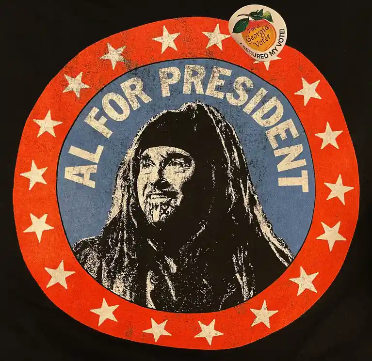 A black t-shirt features a circular political graphic with a red outer ring adorned with white stars, a blue inner circle…