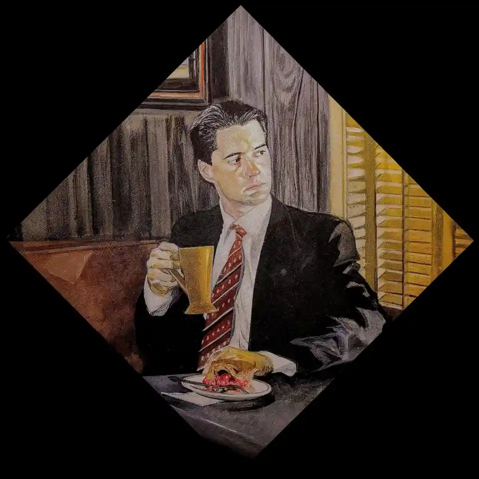A man in a suit and tie sits at a table holding a mug, looking away with a disapproving expression. In front of him is a…