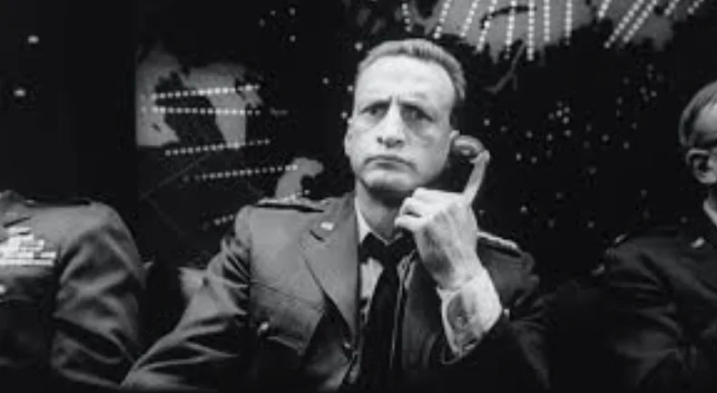 a black and white photo of a man in a military uniform holding a phone to his ear, looking serious and slightly skeptical…