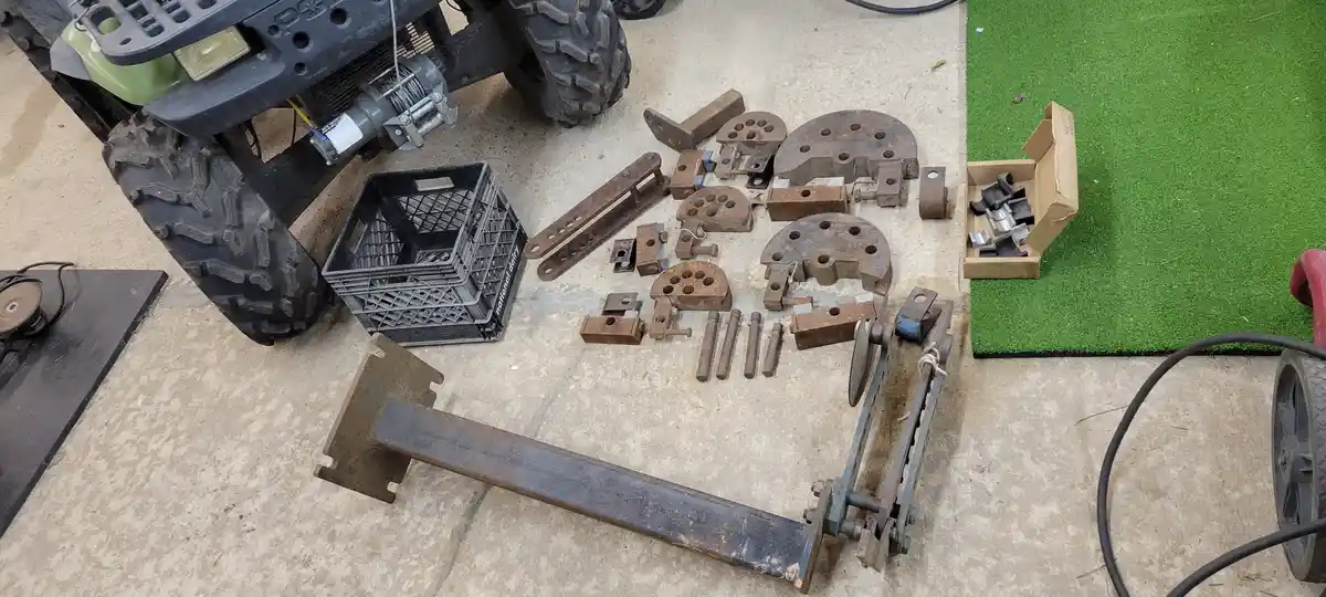 An overhead shot shows a green and black ATV parked on a concrete floor next to a large pile of rusty metal parts, bolts…