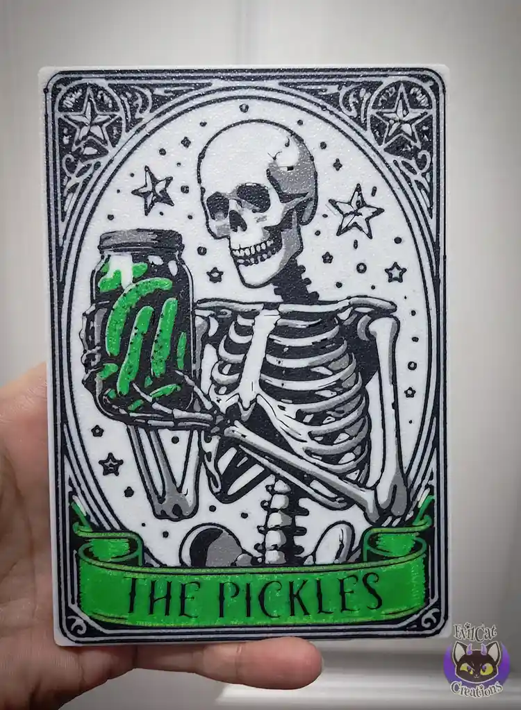 A hand holds a custom tarot card featuring a skeleton holding a jar of green pickles, with stars in the background and a…