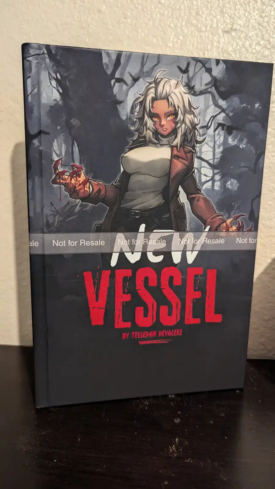 A book titled 'NEW VESSEL' by Tessdan Devalere features a cover illustration of a white-haired, orange-eyed character with…