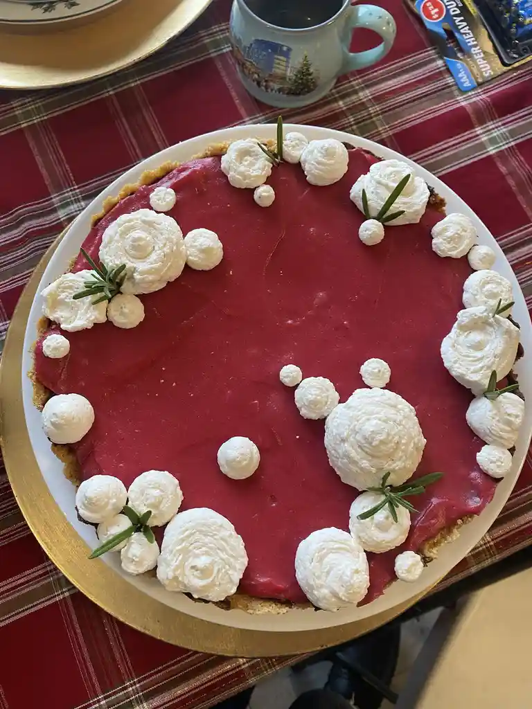 A festive red pie with a golden crust sits on a white plate atop a red plaid tablecloth. The pie is decorated with white…
