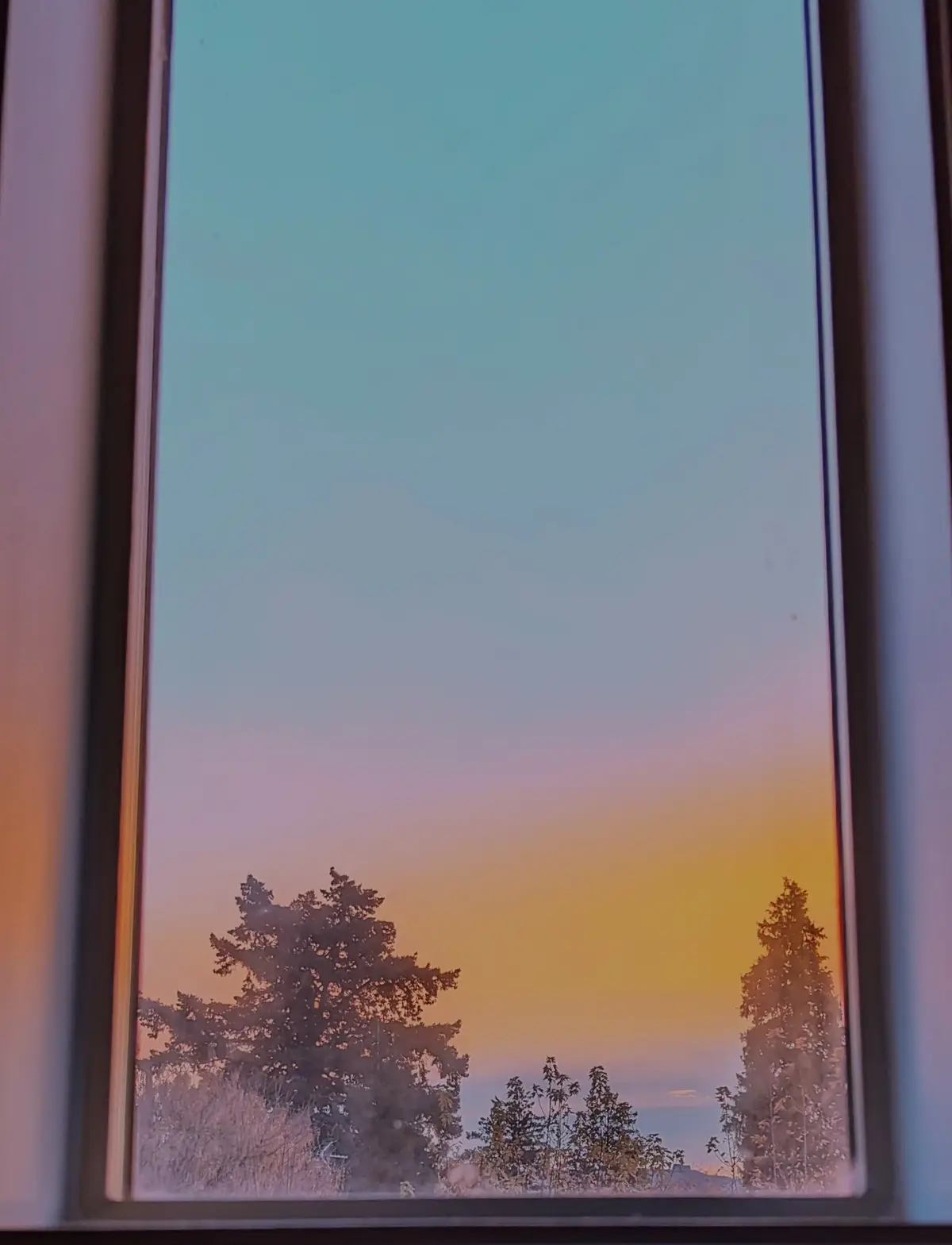 A view through a window shows a serene sunset or sunrise with a gradient sky transitioning from teal to orange, silhouetting…
