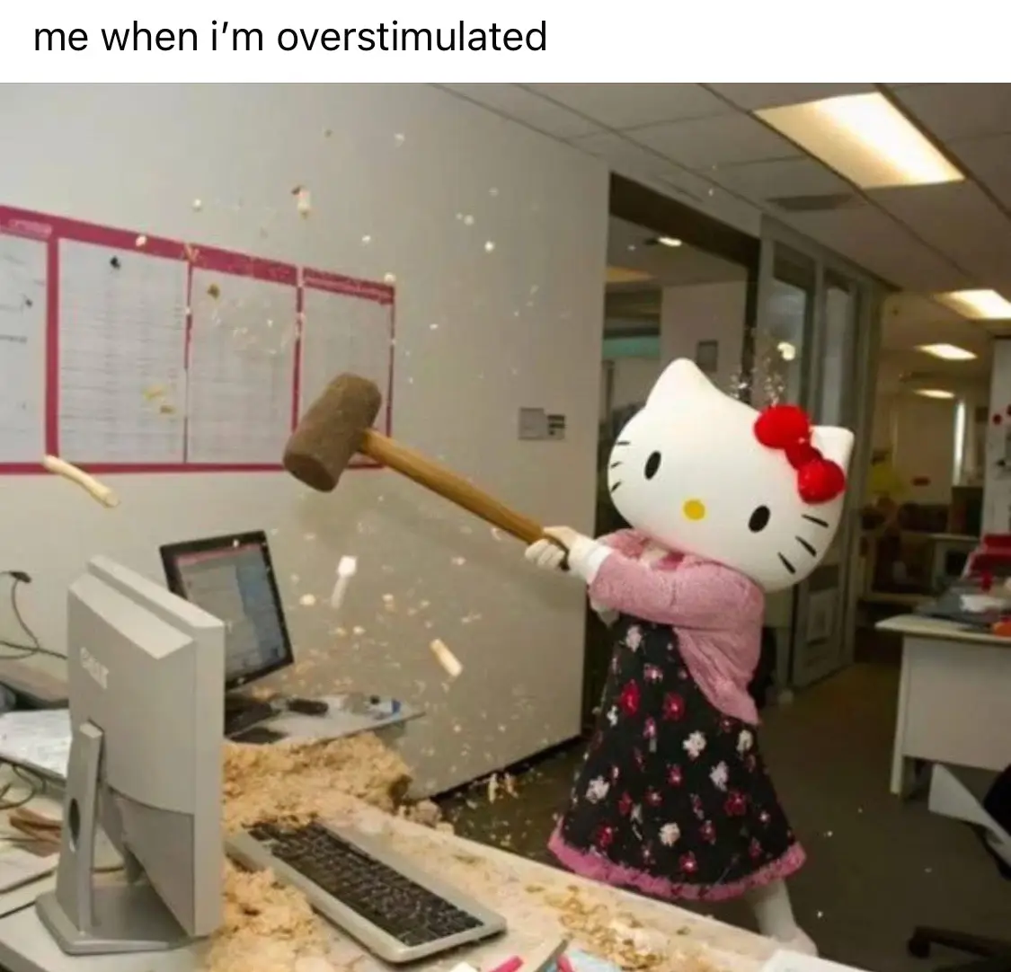 A person in a full-body Hello Kitty mascot costume is shown in an office environment, swinging a large wooden mallet with…