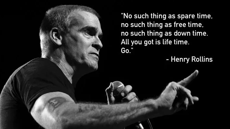A black and white photo of Henry Rollins speaking into a microphone while pointing forward. White text overlaid on the right…