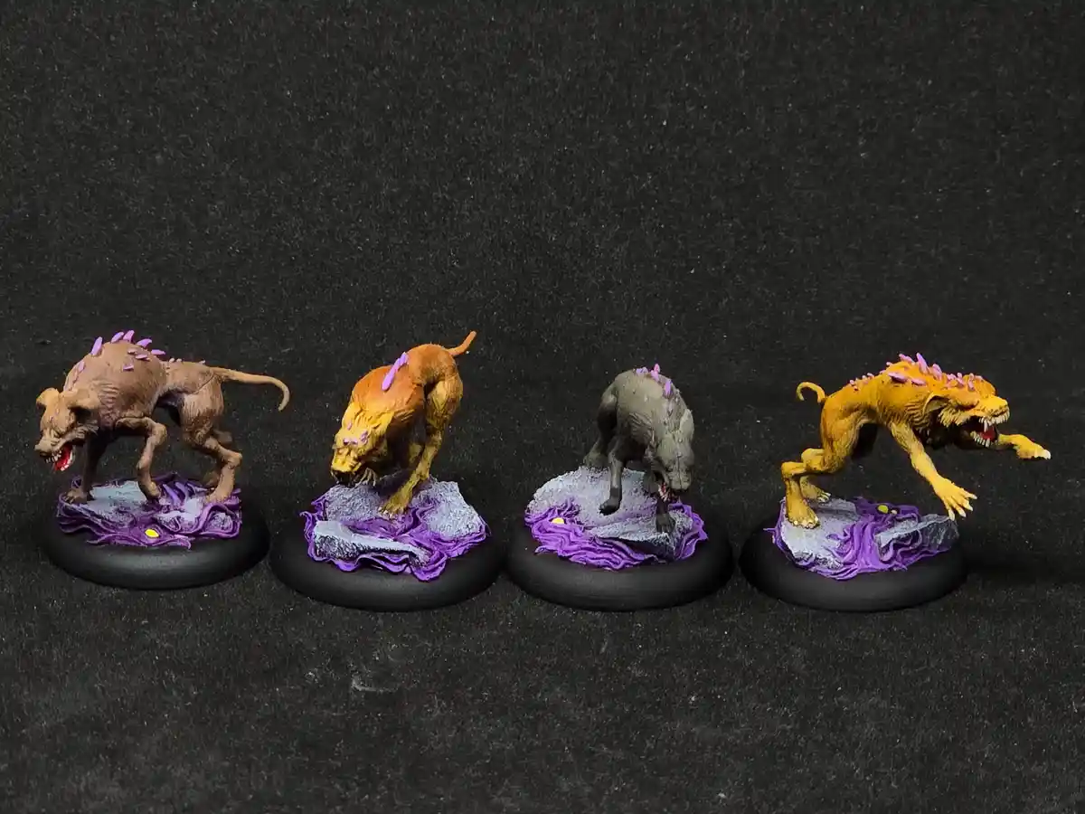 Four painted fantasy miniatures of monstrous, dog-like creatures with purple spikes stand in a row on black circular bases…