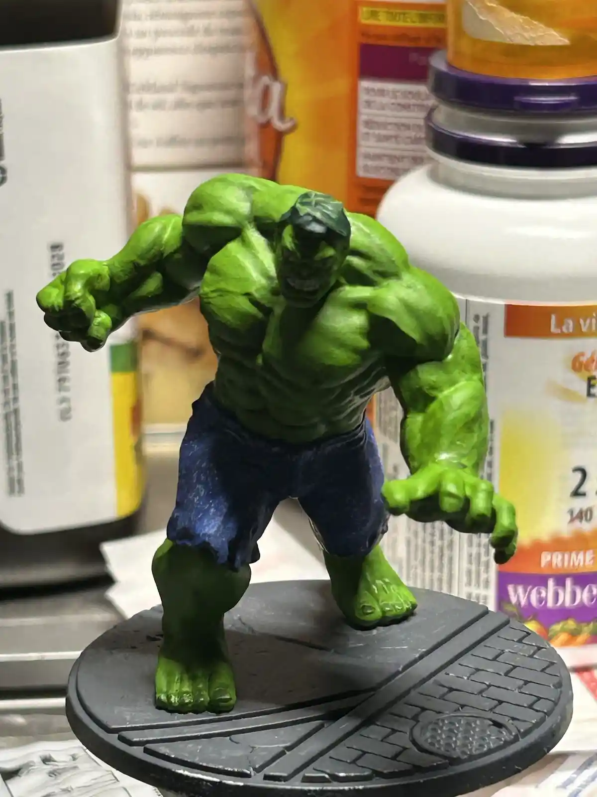 A green, muscular Hulk action figure stands on a black circular base, posed aggressively with fists clenched, surrounded by…