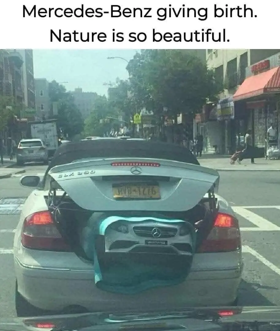 A silver Mercedes-Benz SLK 350 convertible is parked on a city street with its trunk open, revealing a smaller Mercedes-Benz…