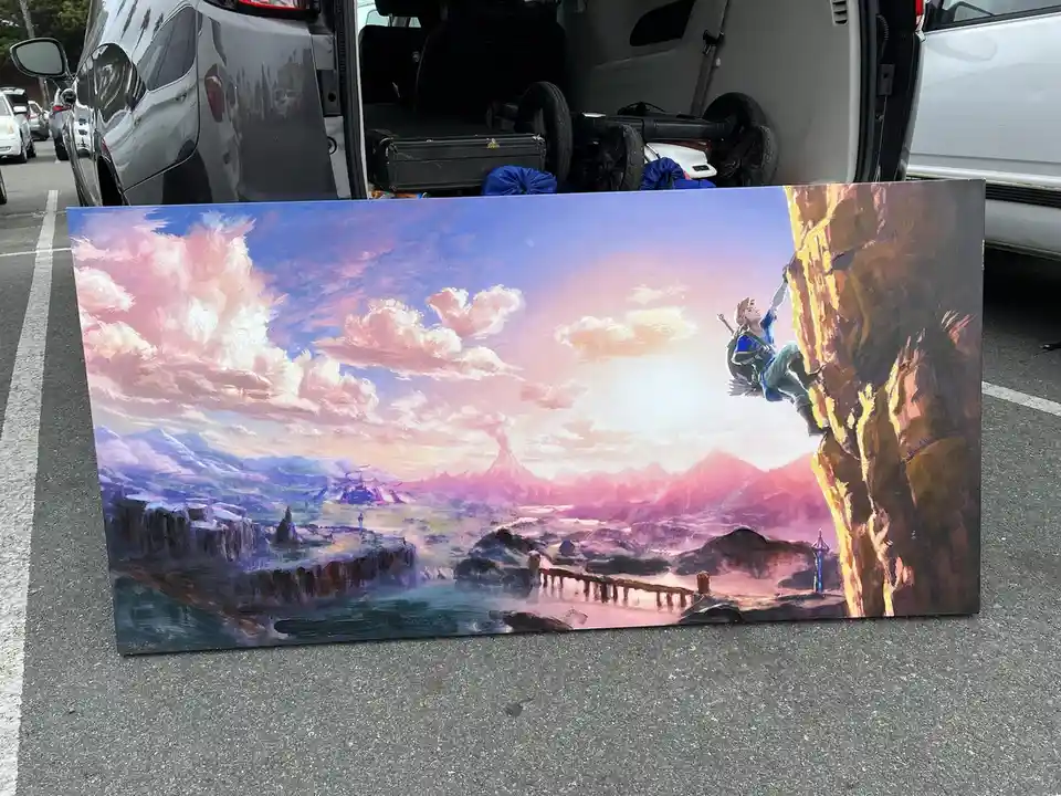 A large, colorful painting of a video game character, Link from The Legend of Zelda, is propped up on asphalt in a parking…
