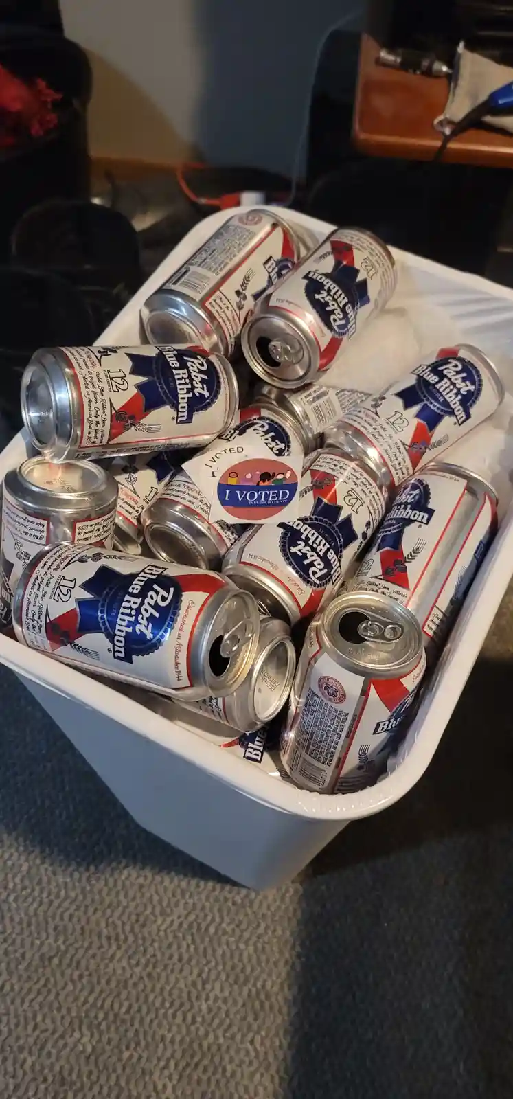 A white cooler is filled with numerous opened cans of Pabst Blue Ribbon beer, with a single 'I VOTED' sticker prominently…