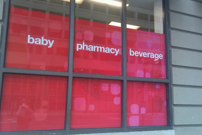 A storefront window divided into six panes, each with a red background and white text. The top row reads 'baby', 'pharmacy'…