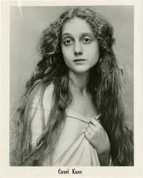 A vintage black-and-white portrait of actress Carol Kane, showing her with long, wavy hair and a neutral expression, wearing…