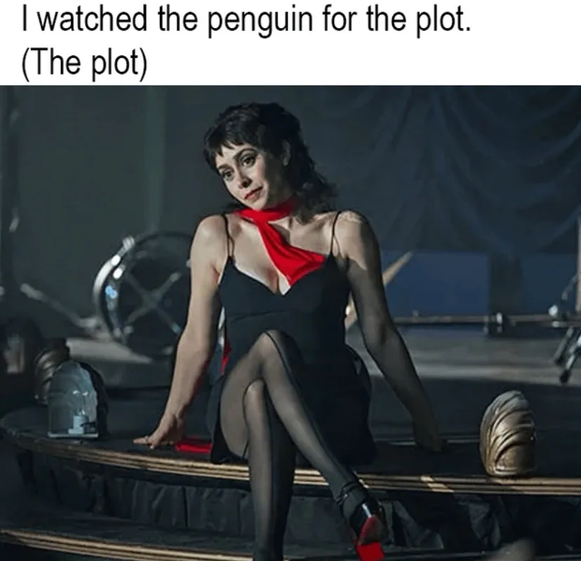 A woman in a black dress with a red scarf sits on a stage-like platform, looking directly at the camera. The overlaid text…