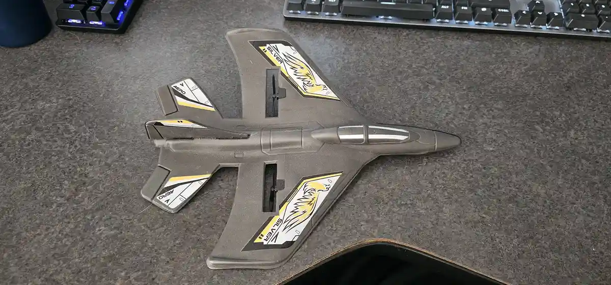 A gray toy jet with yellow and white decals featuring an eagle and the words 'SILVER' and 'AERO' lies on a gray desk next to…