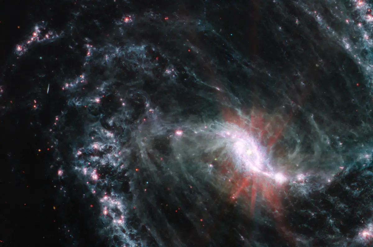 A cosmic image of a spiral galaxy with bright central regions and swirling arms of blue and red gas clouds against a black…